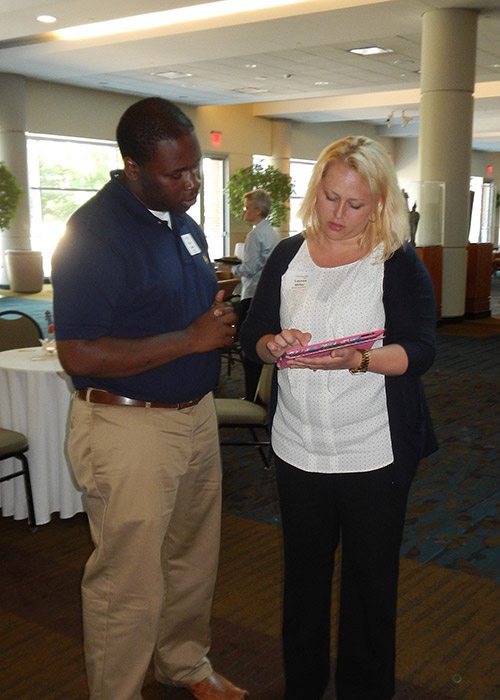 Lauren Miller of Moxley Carmichael demonstrates the site to Ryan Parker, assistant program director for the Wesley House. Maria Cornelius of Moxley Carmichael is in the background discussing the site with another attendee.