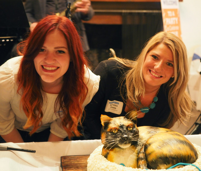 Moxley Carmichael interns Lindsey Collins, left, and Savanna Howie, enjoyed a 3D replica cake of Rexie - the beloved cat of Cynthia Moxley - at Moxley's 60th birthday party earlier this year. Collins is now with the International Biscuit Festival in Knoxville, and Howie has accepted a job with a public relations firm in Nashville.